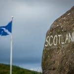 A Stone Sign At The Scottish Border With A Scotland Flag In The